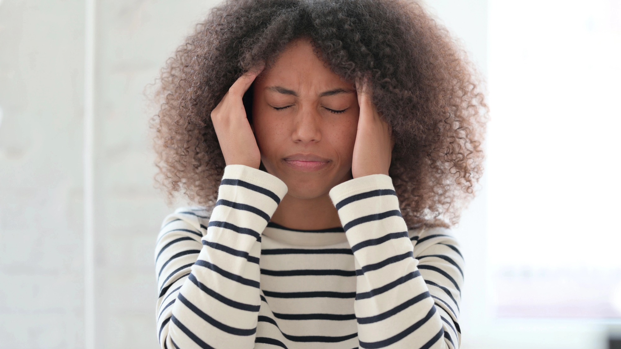 Woman in stripped shirt experiencing Temporal Migraine headache Woman in stripped shirt experiencing Temporal Migraine